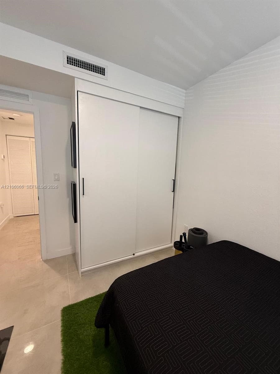 Floor-to-ceiling built-in closet with sliding panels, minimalist white cabinetry, and light-toned tile flooring