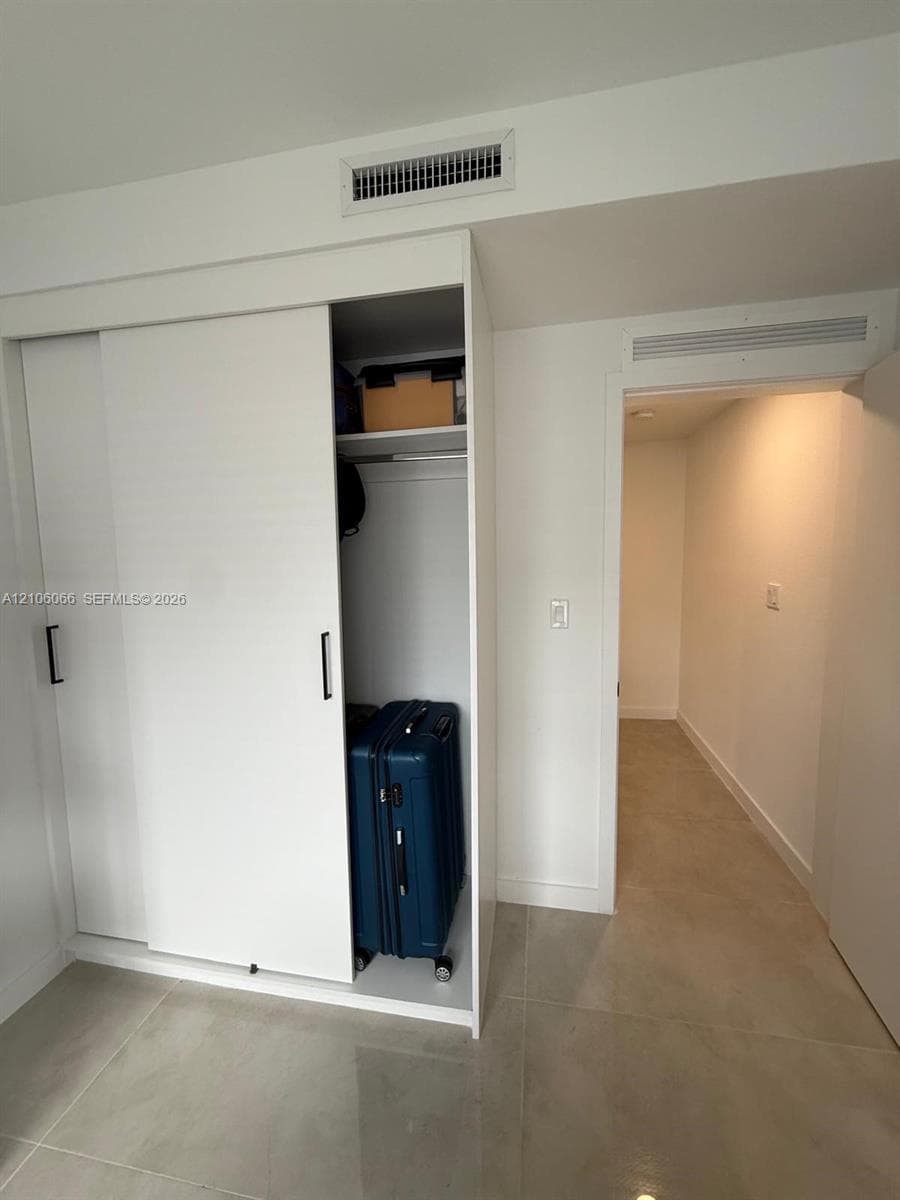 Built-in sliding-door closet featuring white cabinetry, integrated shelving, and matte black hardware with polished stone-finish flooring