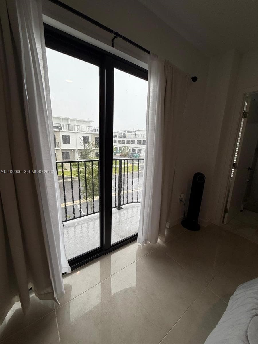 Full-height glass door with black frame, tiled flooring, and a private balcony featuring a black metal railing