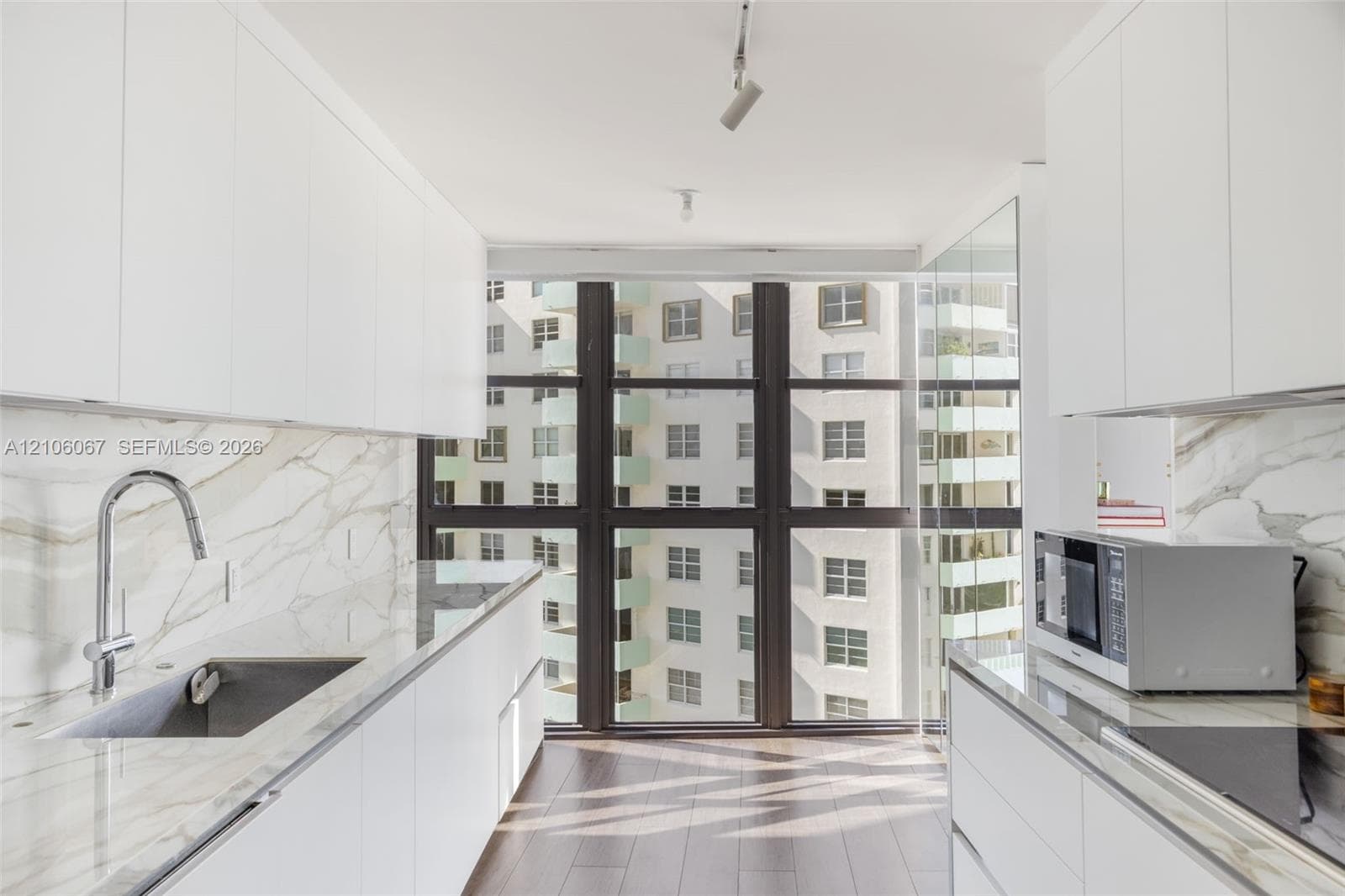 Kitchen featuring white flat-panel cabinetry, floor-to-ceiling windows, veined stone-finish countertops and backsplash, wood-finish flooring, and a stainless steel undermount sink with a gooseneck faucet