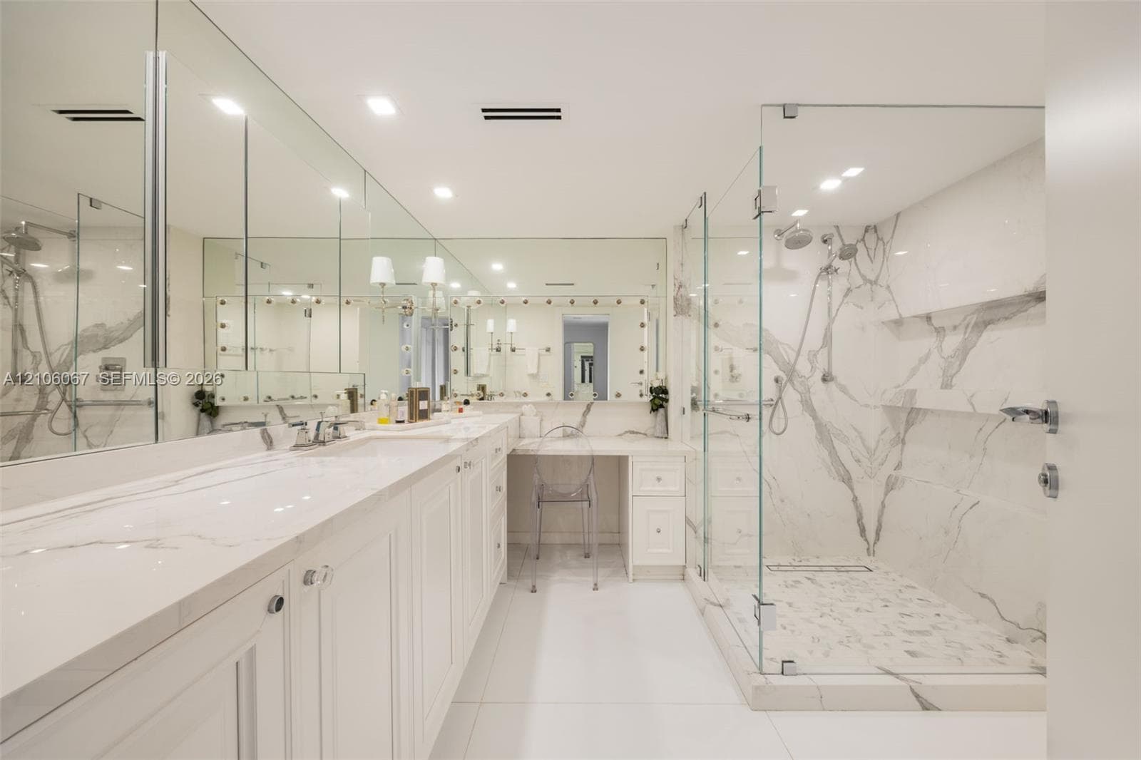 Dual-sink vanity with quartz countertop, expansive wall-to-wall mirrors, integrated makeup vanity station, and glass-enclosed walk-in shower featuring floor-to-ceiling stone wall cladding