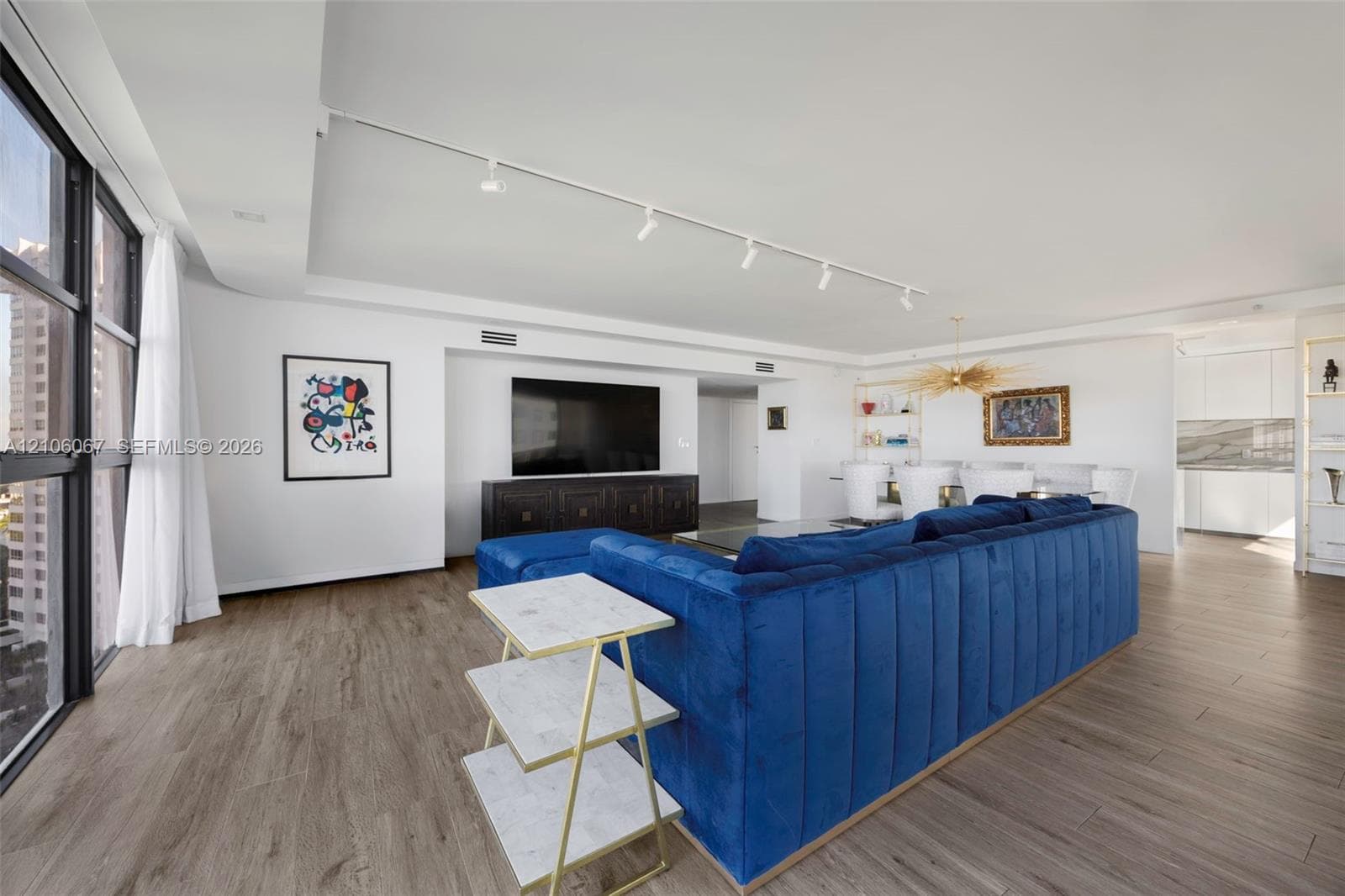 Modern kitchen featuring white flat-panel cabinetry, stone-finish countertops and backsplash, integrated refrigerator, undermount sink with high-arc faucet, and wood-finish flooring