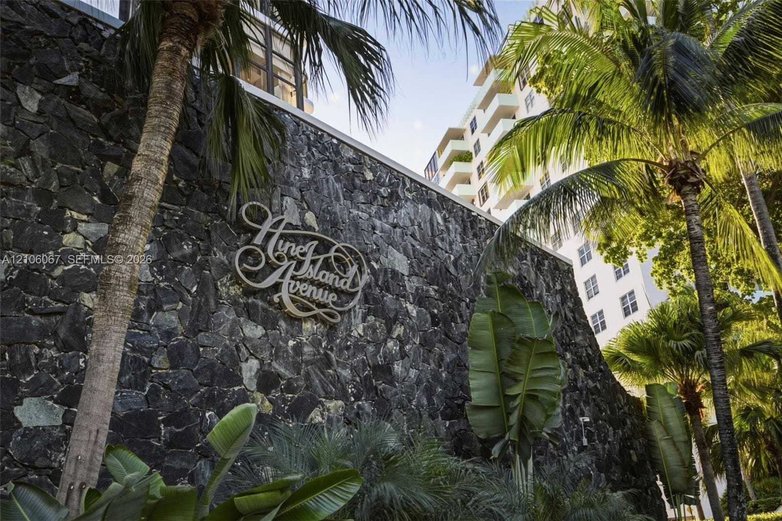 Natural stone masonry wall featuring custom metal signage, accented by mature palm trees and tropical landscaping