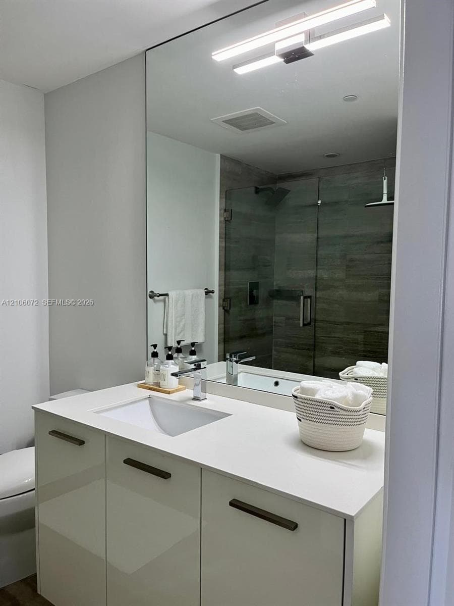 Modern vanity featuring a white composite countertop, integrated rectangular sink, and gloss-finish cabinetry with linear pulls