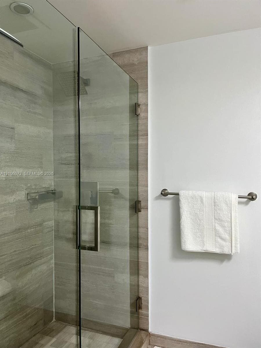 Walk-in glass shower featuring tile walls, built-in metal shelving, a square rain-style showerhead, and a mounted metal towel bar