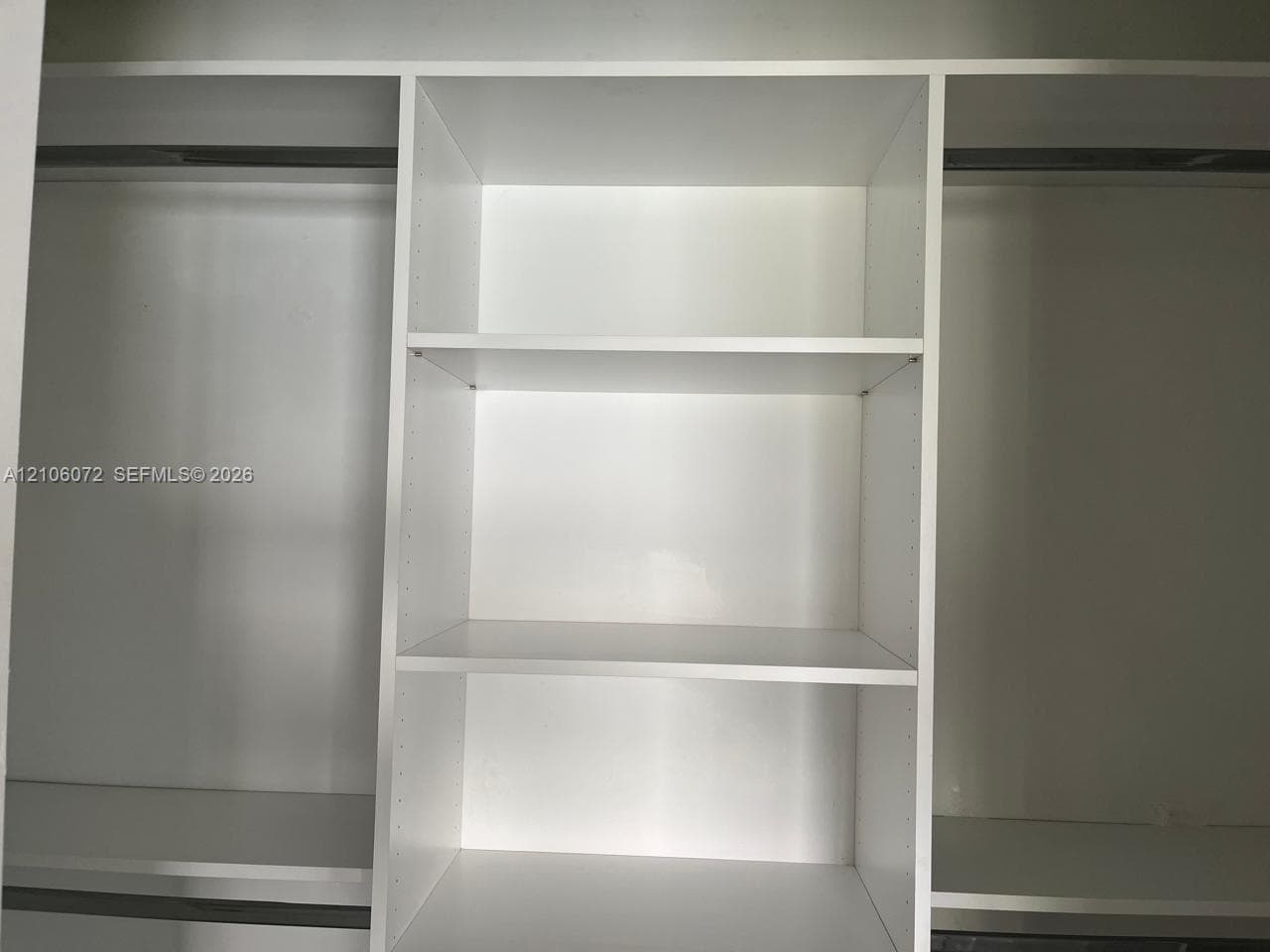Built-in closet organizer featuring white laminate shelving, a center tower with fixed storage compartments, and integrated garment rods