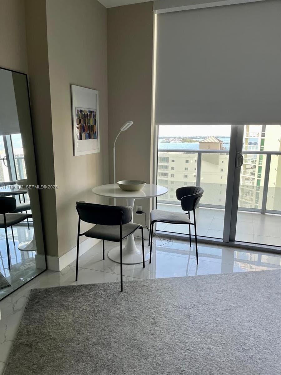 Floor-to-ceiling sliding glass doors with roller shades, white polished tile flooring, and a private balcony featuring a metal railing