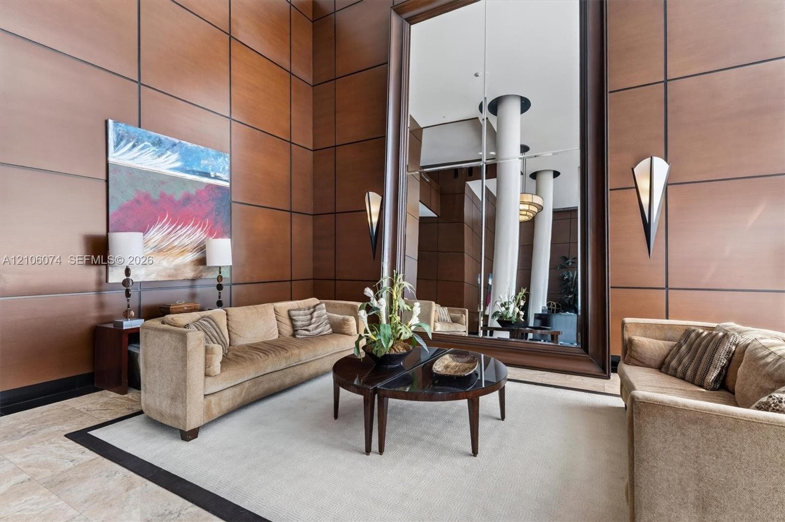 Double-height interior featuring wood-panelled wall treatments, oversized framed mirror, and integrated triangular wall sconces