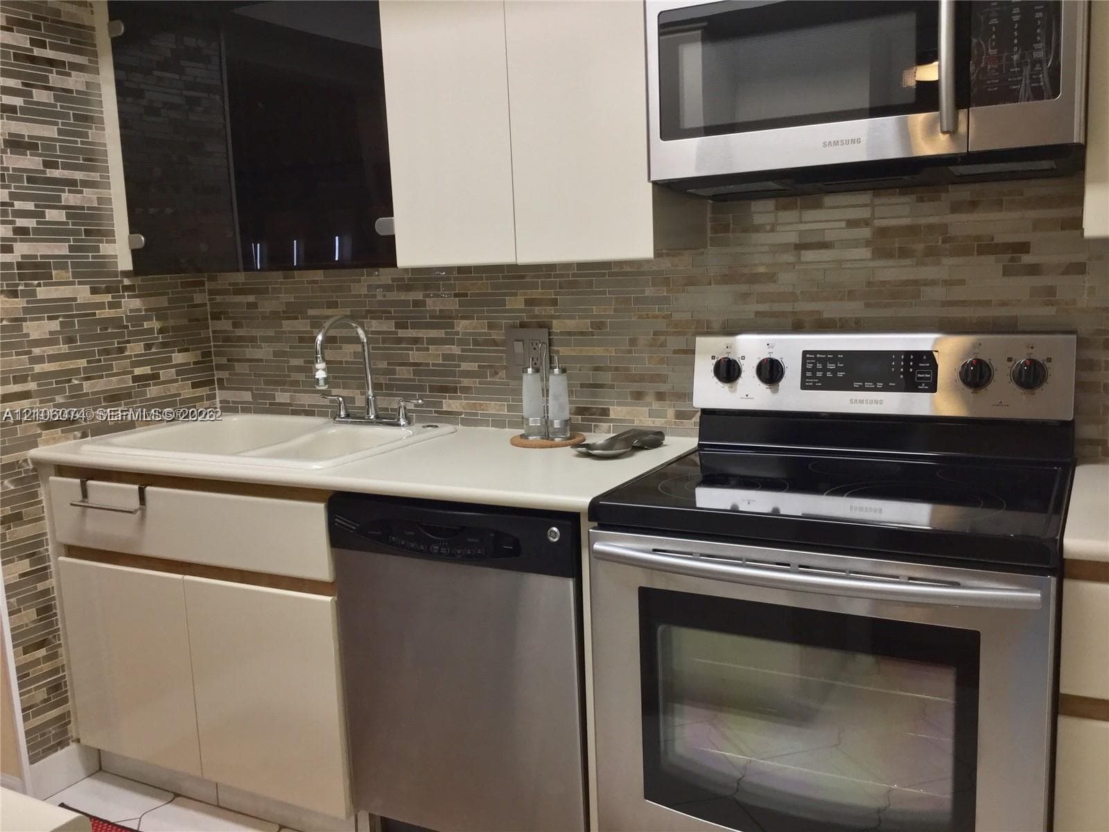 Kitchen featuring stainless steel appliances, dual-basin sink with arched faucet, mosaic tile backsplash, and two-tone flat-panel cabinetry