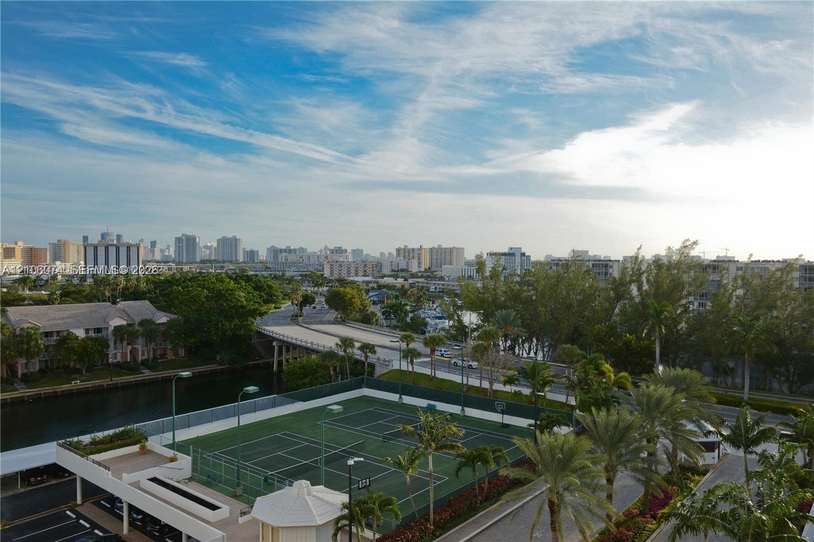 Tennis court featuring fenced perimeter, integrated lighting, and palm-lined landscaping