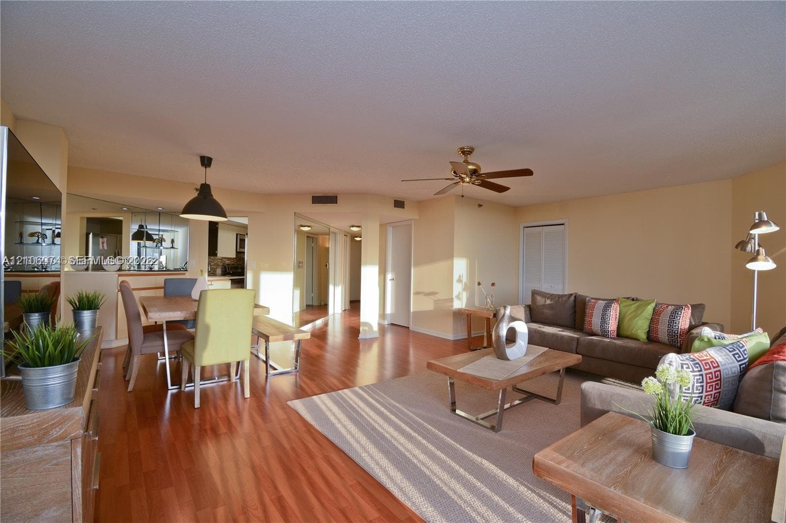 Open-concept living area featuring wood-finish flooring, recessed lighting, ceiling fan, and mirrored wall accents