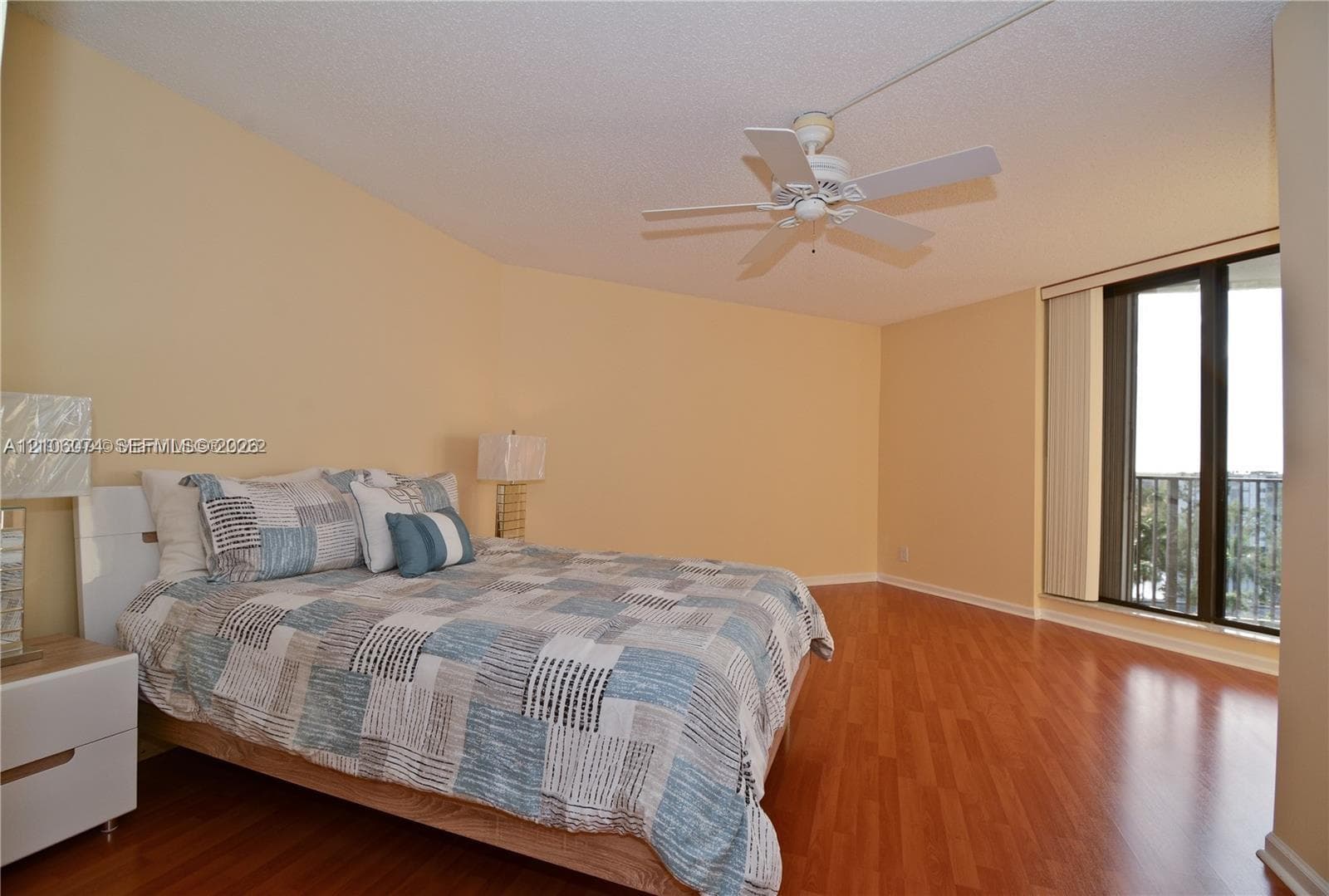Room featuring wood-finish flooring, a white ceiling fan with integrated lighting, and glass sliding doors providing access to an exterior balcony