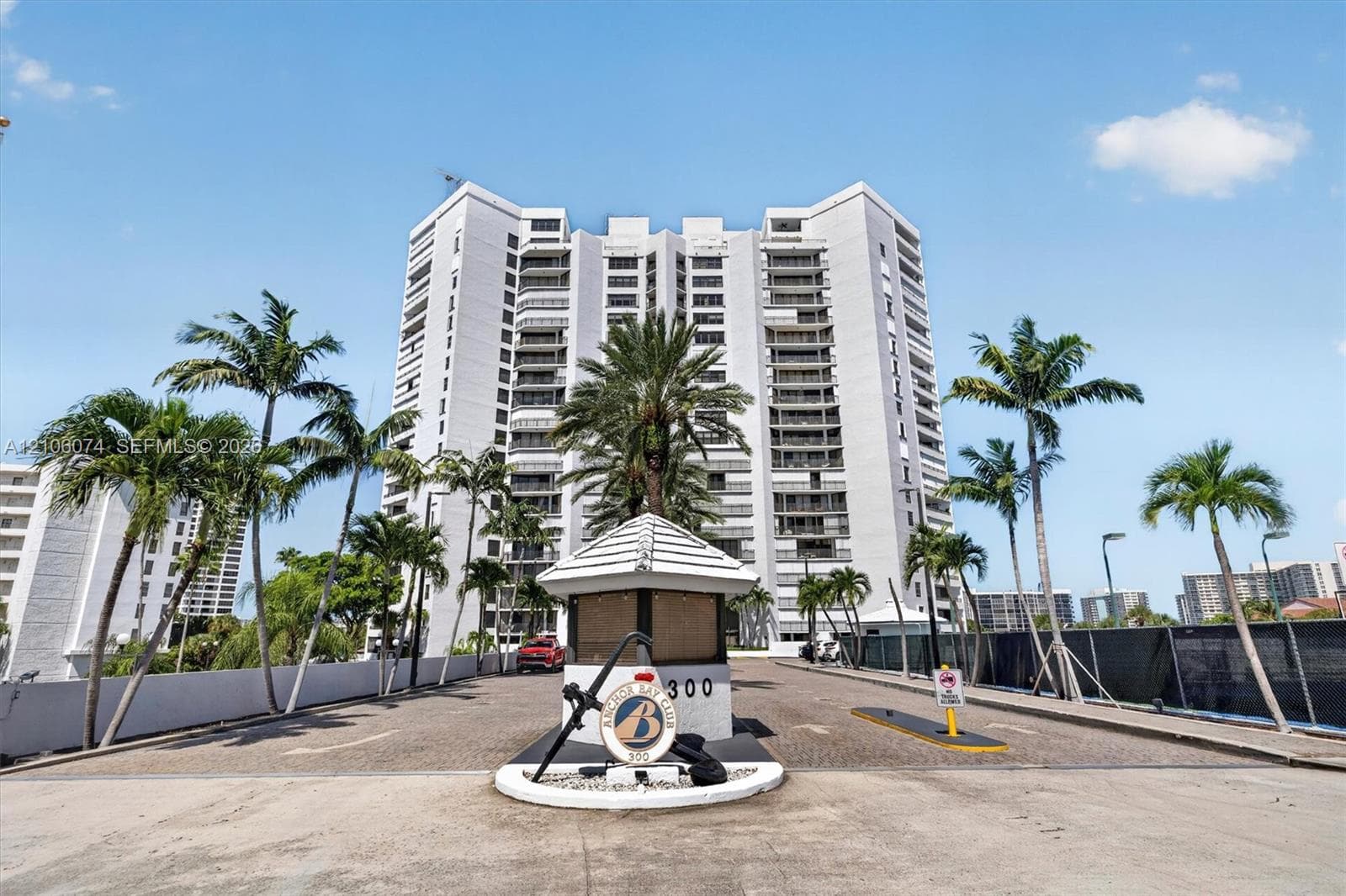 Multi-story residential high-rise featuring a secure gated entrance with guardhouse, paved arrival area, and mature palm landscaping