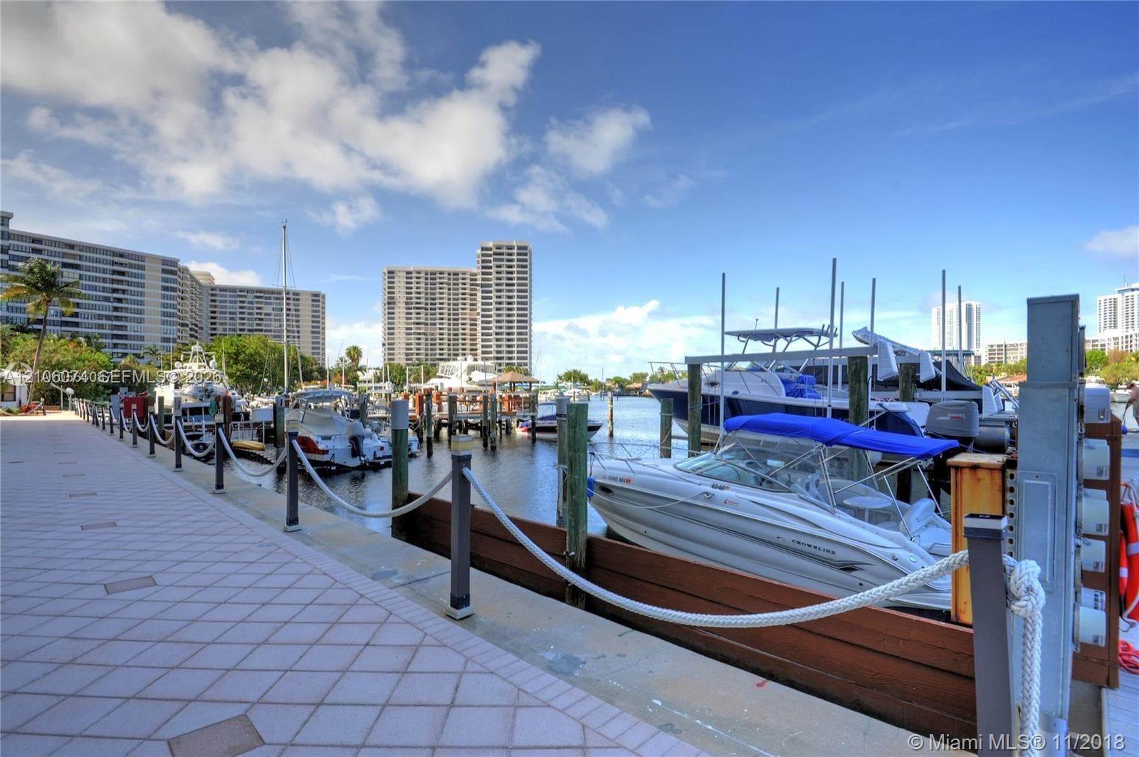 Waterfront boat slip featuring wood bulkhead, dockside pedestals, and rope railing with metal posts along a paved promenade