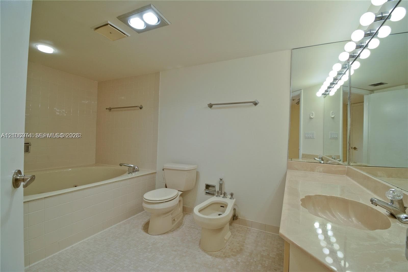 Bathroom featuring a stone-surface vanity with an integrated scalloped sink, large wall-mounted mirror, deep soaking tub with tile surround, and a bidet