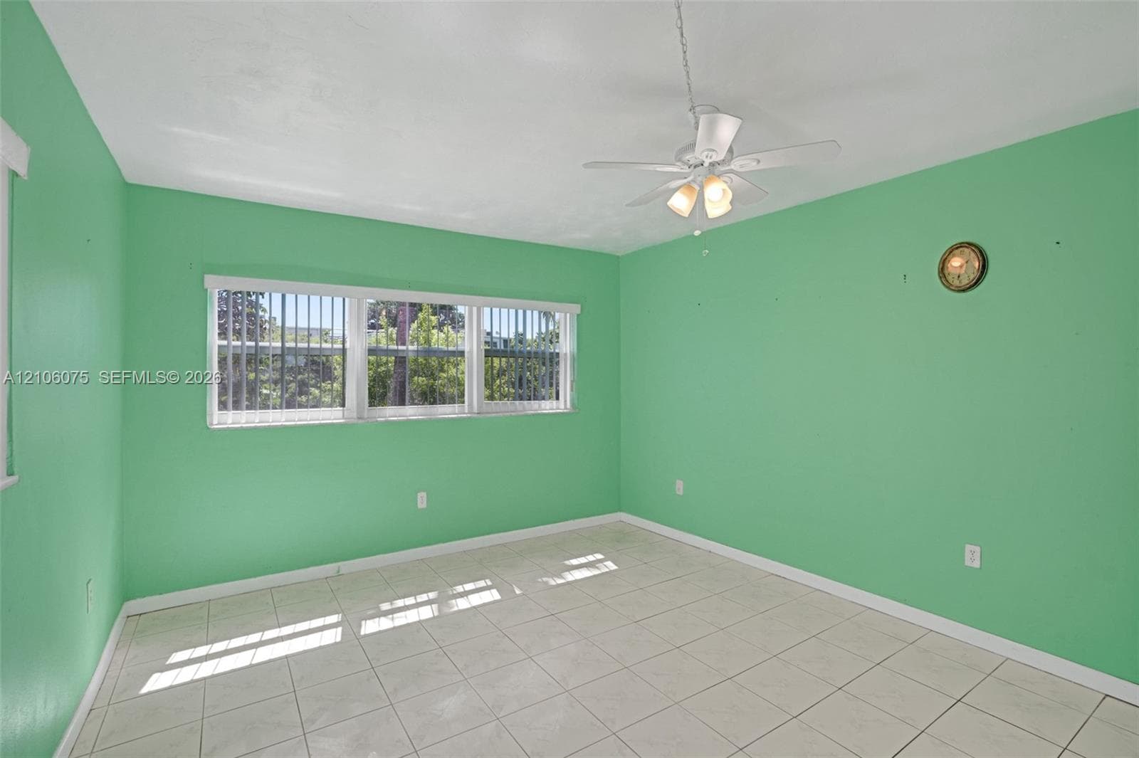 Room featuring light-toned tile flooring, a horizontal multi-pane window with vertical blinds, and a white ceiling fan with integrated lighting