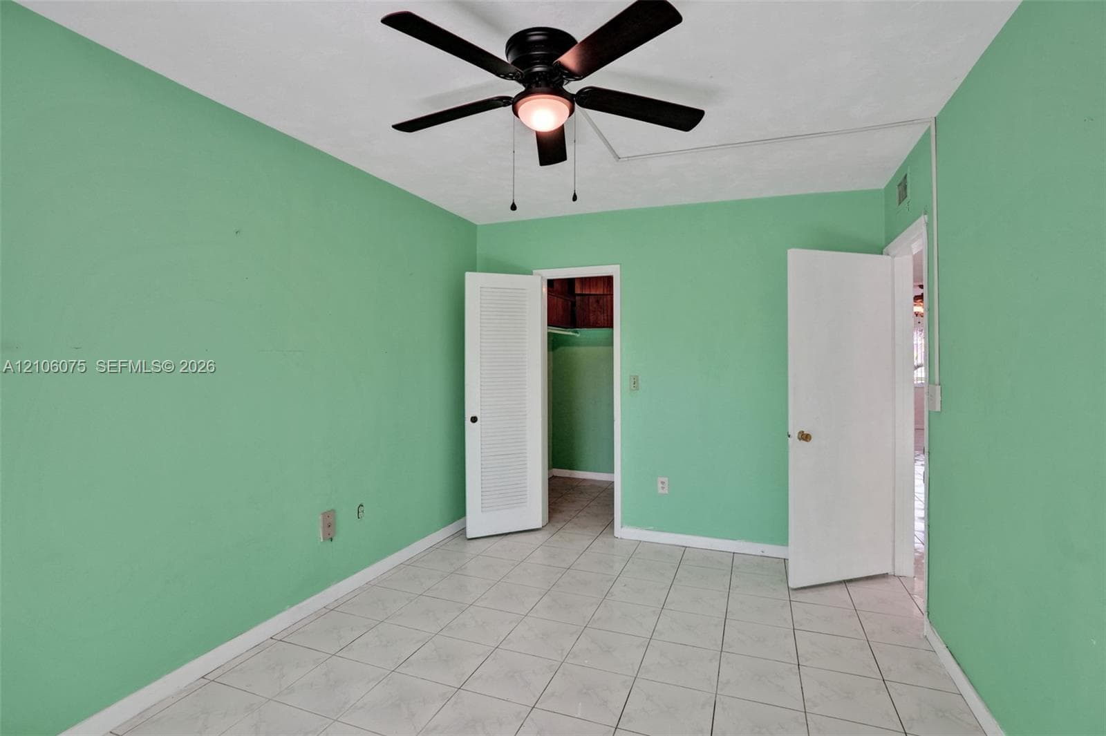 Room featuring large-format ceramic tile flooring, a centered ceiling fan with integrated lighting, and louvered closet doors