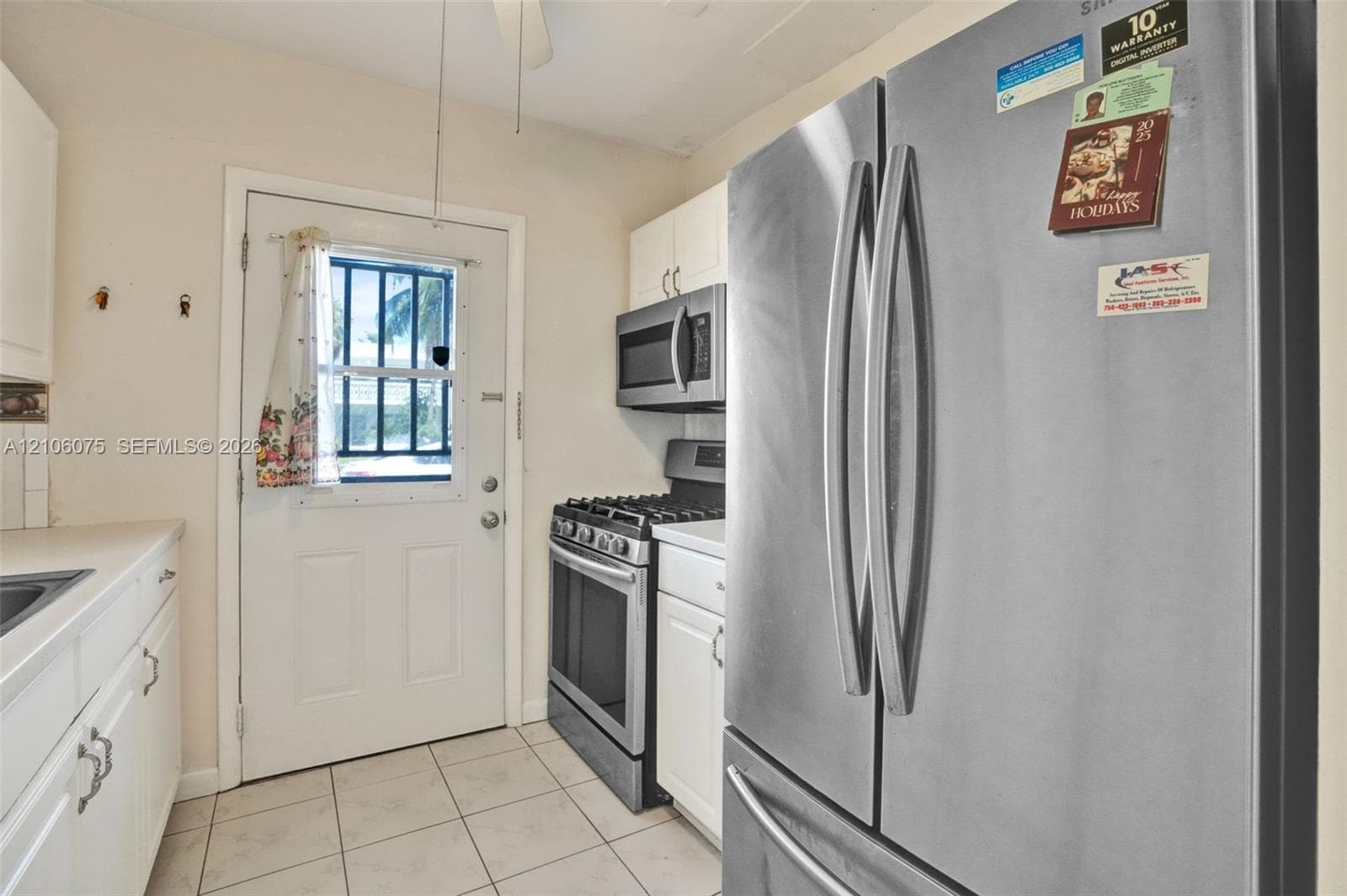 Kitchen featuring white cabinetry, stainless steel French door refrigerator, gas range, over-the-range microwave, and tile flooring