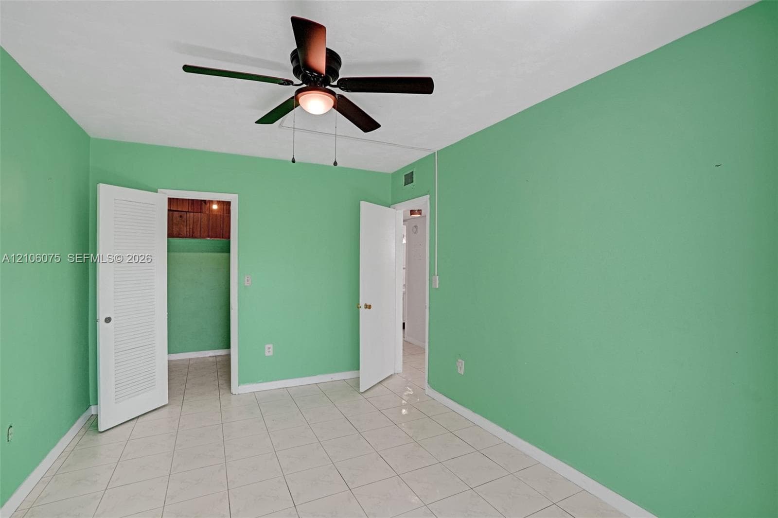 Interior space featuring neutral tile flooring, a central ceiling fan with integrated lighting, and louvered closet doors