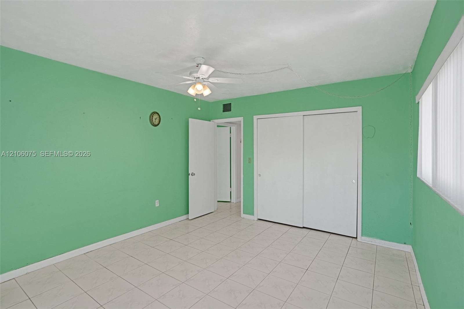 Room featuring ceramic tile flooring, ceiling fan with integrated lighting, dual-panel sliding closet doors, and vertical window blinds