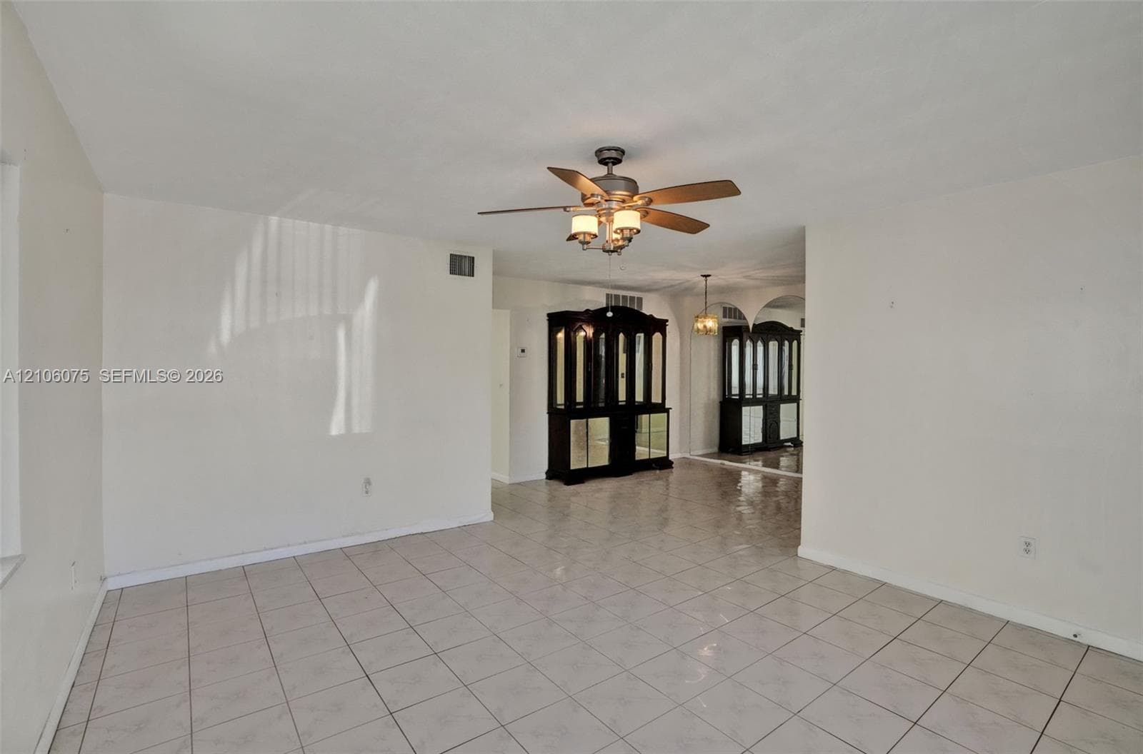 Neutral tile flooring, ceiling fan with integrated lighting, and built-in cabinetry featuring glass display doors