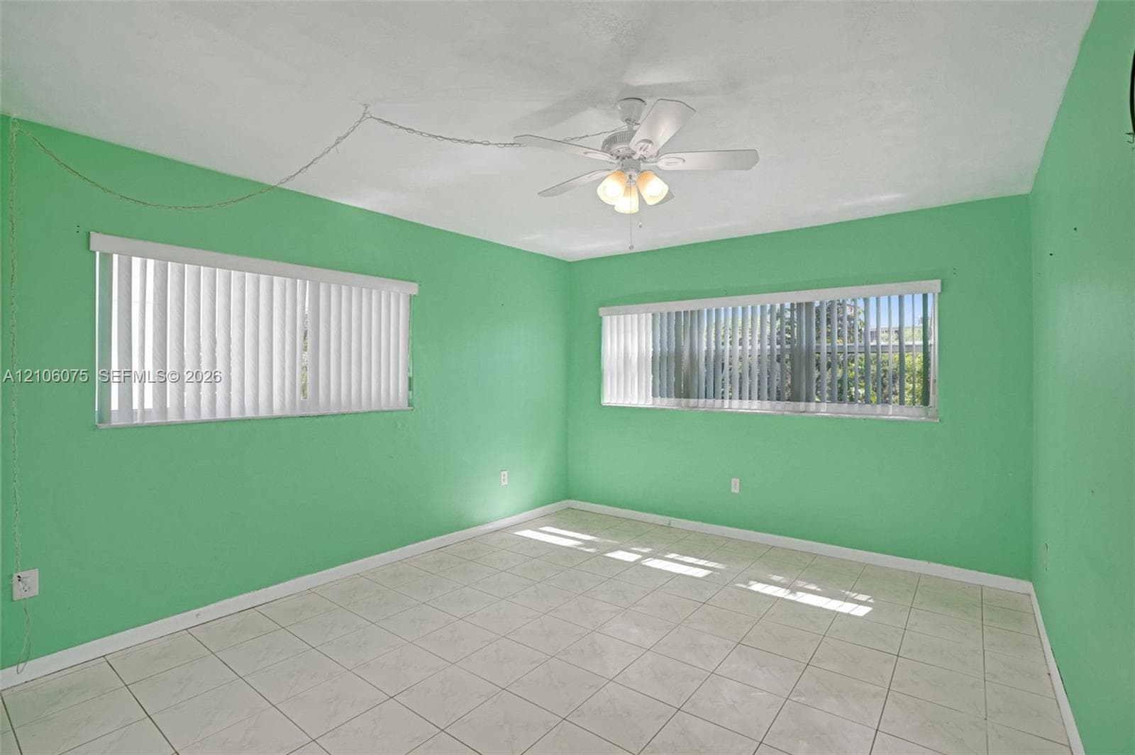 Room featuring tile flooring, two windows with vertical blinds, and a ceiling fan with light fixture
