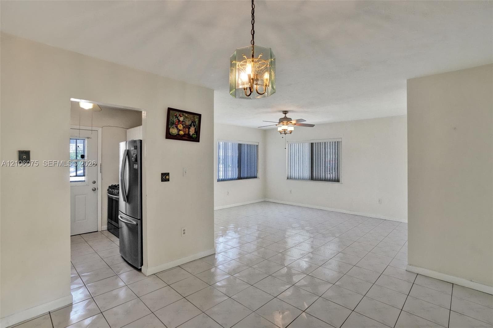Neutral-toned interior featuring ceramic tile flooring, a geometric glass pendant light fixture, a ceiling fan with integrated lighting, and vertical window blinds