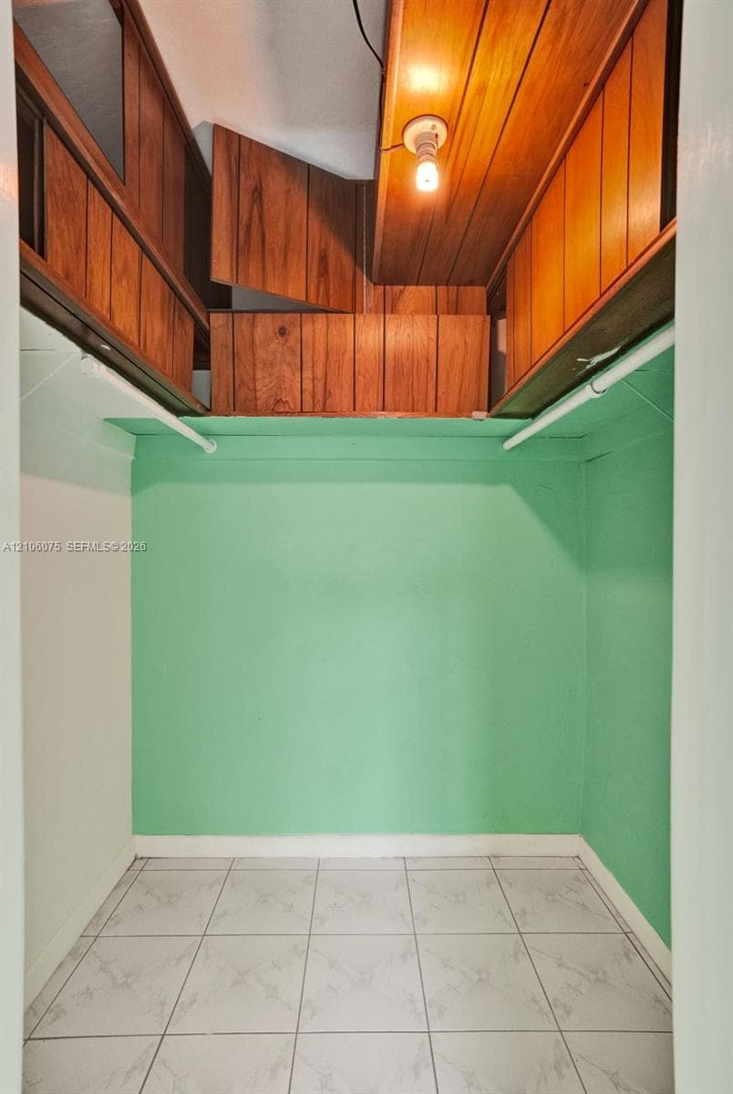 Storage area featuring overhead wood-paneled cabinetry, tiled flooring, and dual mounted garment rods