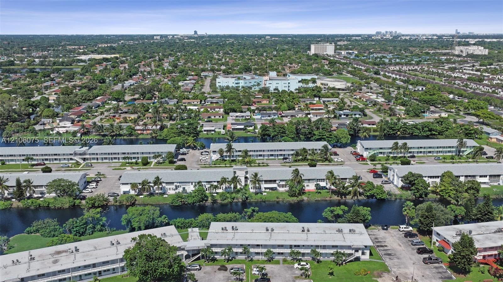 Aerial perspective of multi-family structures featuring paved surface parking, low-pitched rooflines, integrated balconies, and waterfront property positioning within a suburban landscape