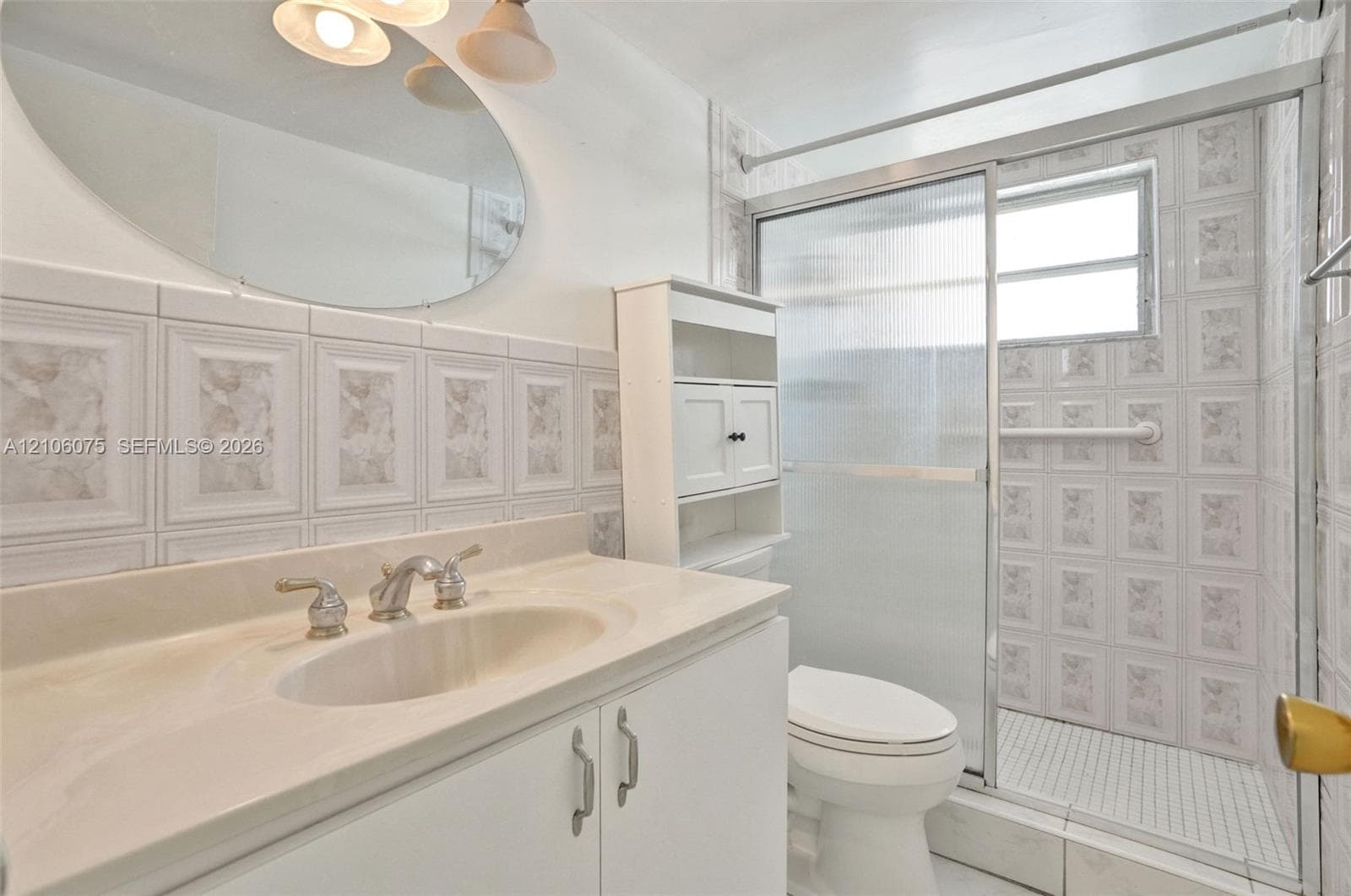 Bathroom featuring a white vanity with a composite countertop and integrated basin, oval wall-mounted mirror, built-in storage shelving, and a tiled shower enclosure with sliding glass doors