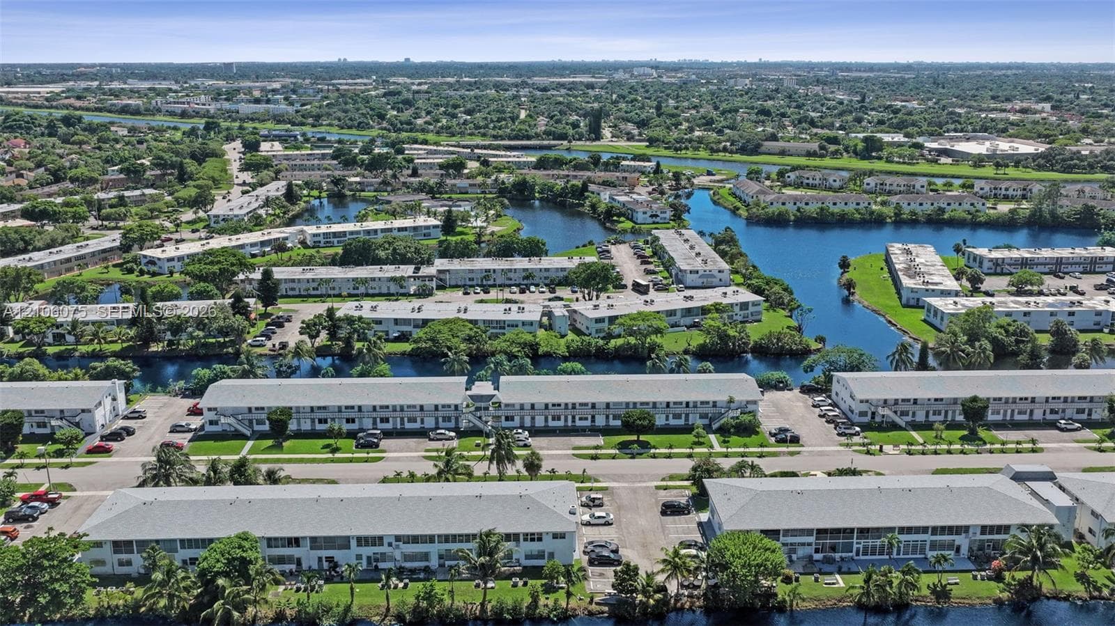 Aerial perspective of multi-family structures featuring pitched shingle roofing, paved surface parking, integrated canal systems, and mature palm trees