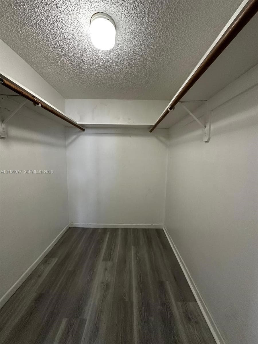 Storage area featuring wood-finish flooring, white walls, integrated shelving, and ceiling-mounted lighting