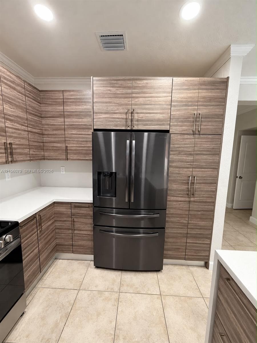 Kitchen featuring horizontal-grain wood cabinetry, ceiling-height pantry storage, white solid-surface countertops, recessed lighting, and a stainless steel French-door refrigerator