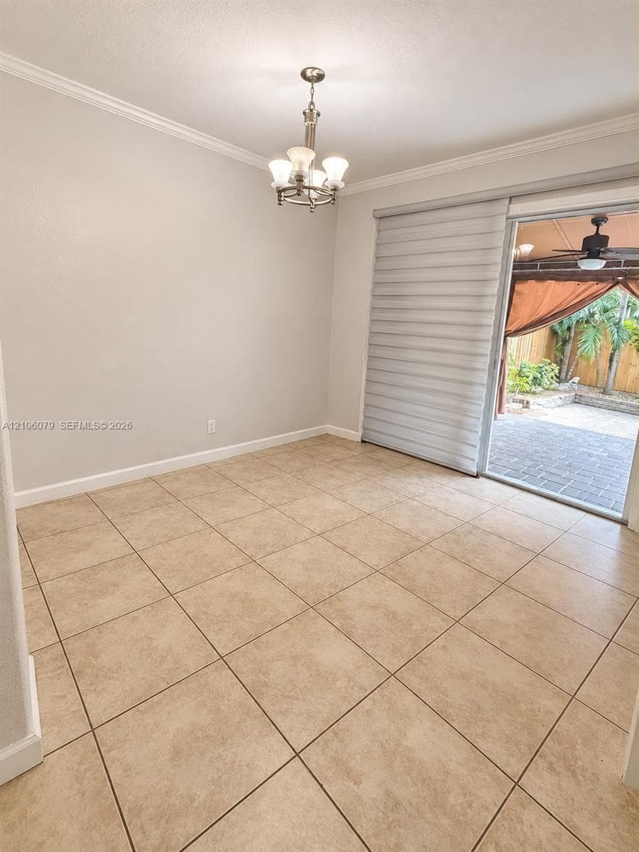 Neutral-toned tile flooring, crown molding, multi-light chandelier, and sliding glass door with integrated window treatments