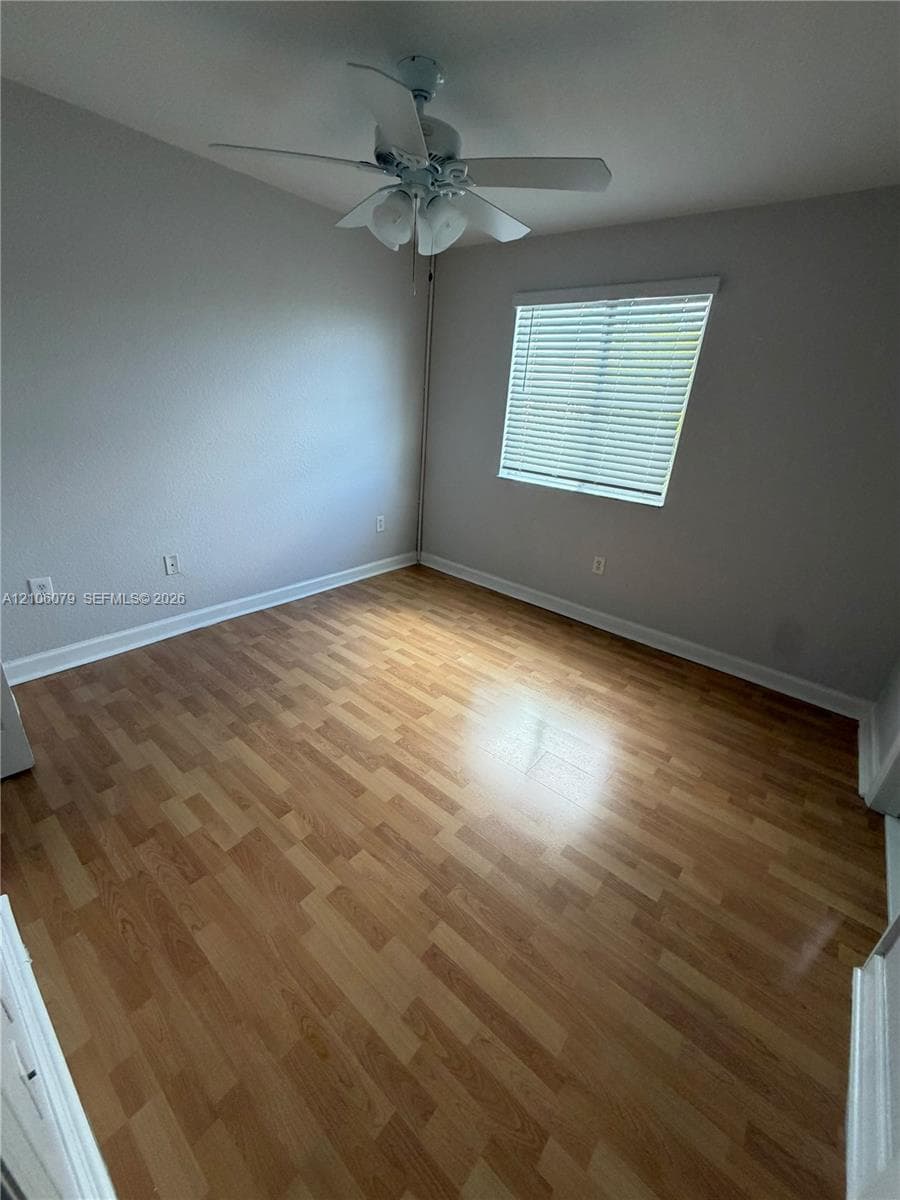 Room featuring wood-finish flooring, neutral wall paint, and a ceiling-mounted fan with integrated lighting