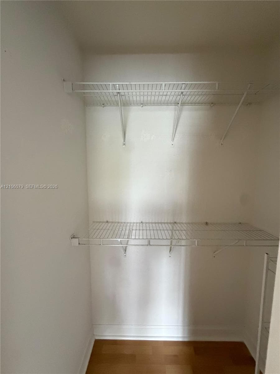 Closet interior featuring two levels of built-in white wire shelving and wood-finish flooring