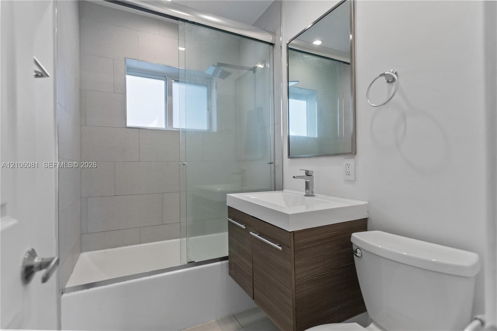 Floating vanity with wood-finish cabinetry, rectangular integrated sink, glass-enclosed shower, and large-format tile surround
