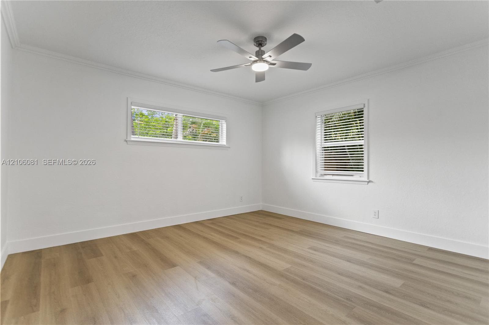 Neutral interior featuring wood-finish flooring, white walls, crown molding, multi-pane windows with horizontal blinds, and a central ceiling fan with an integrated light fixture