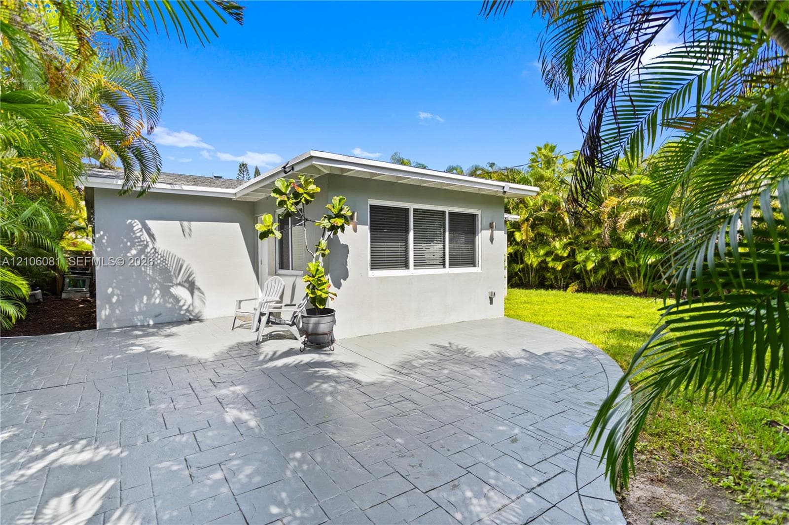 Stamped concrete patio featuring a manicured lawn, low-maintenance exterior, and mature tropical foliage