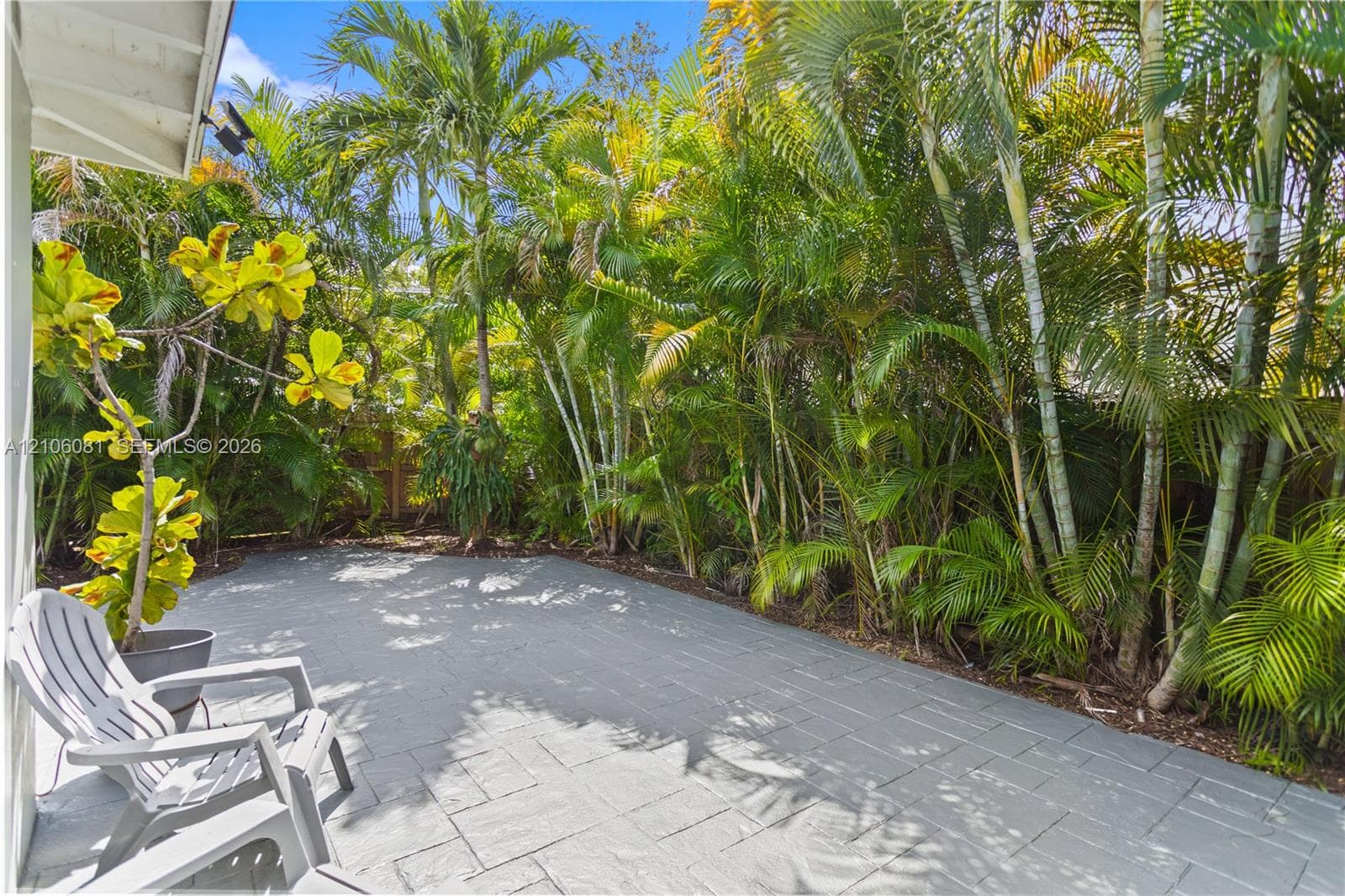 Paver patio with a stone-finish surface, bordered by mature palm trees and established tropical landscaping