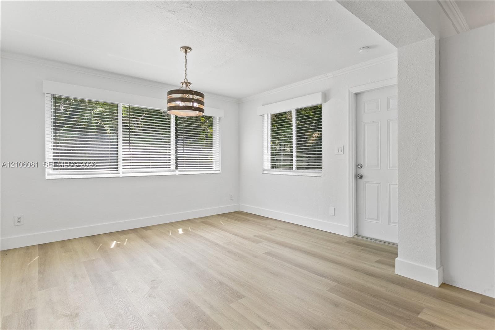 Interior space featuring wood-finish flooring, white walls, multiple windows with horizontal blinds, and a drum-style pendant light fixture