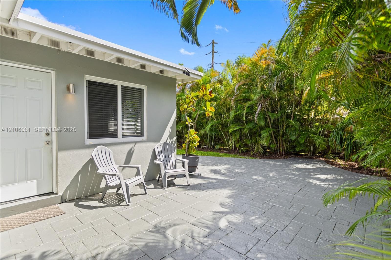 Outdoor patio featuring stone-paver hardscaping, light-grey exterior finish, and mature perimeter landscaping