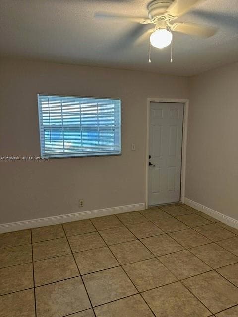 Room featuring neutral wall paint, tile flooring, a horizontal window with blinds, a six-panel door, and a ceiling-mounted light fixture with a fan
