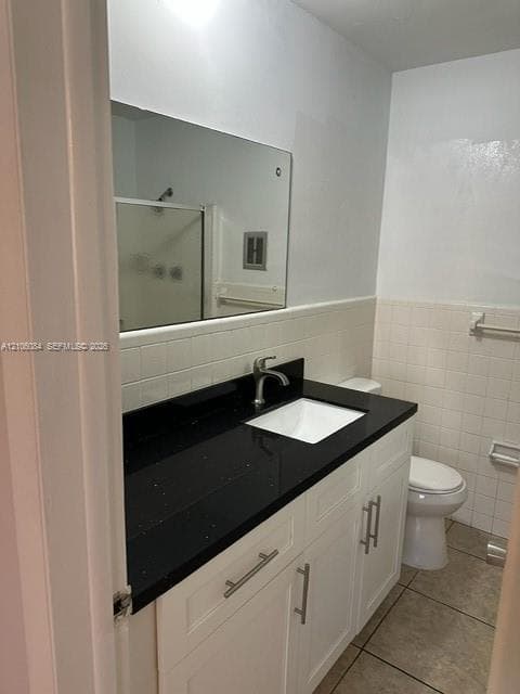 Bathroom vanity featuring a dark stone countertop, integrated rectangular sink, brushed-metal hardware, white cabinetry, and a large frameless mirror