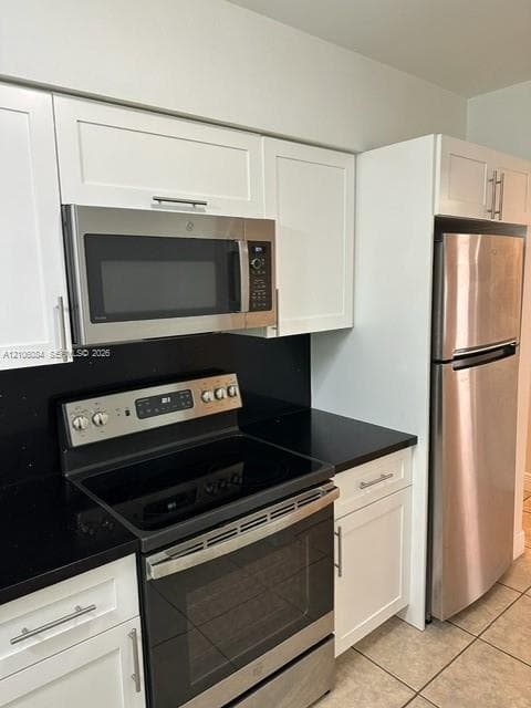 Kitchen featuring white shaker-style cabinetry, black solid-surface countertops, and a suite of stainless steel appliances including a smooth-top range and over-the-range microwave