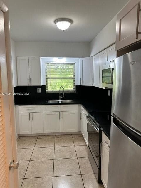 Kitchen featuring white cabinetry, contrasting dark countertops, a double-basin sink, stainless steel appliances, and ceramic tile flooring