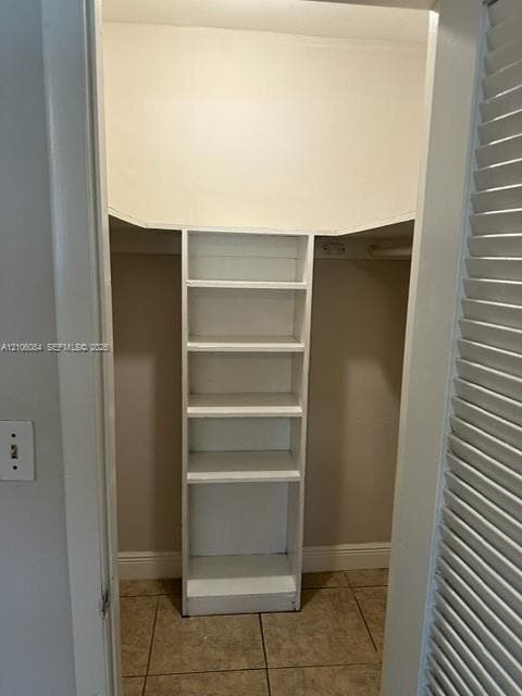Storage space featuring built-in vertical shelving, a horizontal hanging rod, and tile flooring, secured by a louvered bifold door