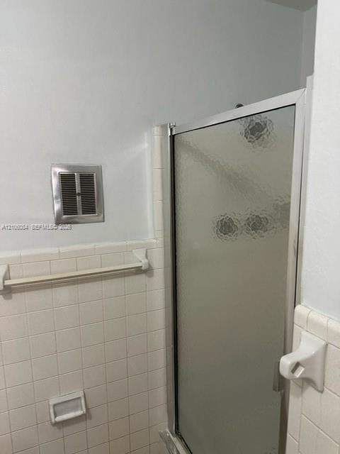 Shower enclosure with textured glass door, white square wall tile, built-in recessed soap dish, and wall-mounted towel bar