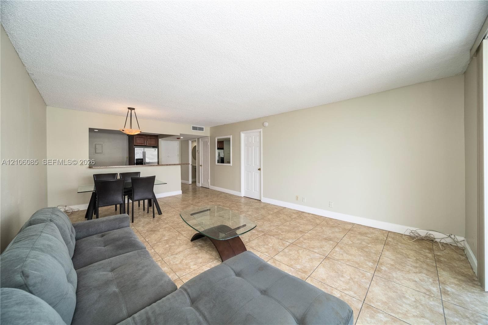 Open-concept interior featuring large-format tile flooring, a pass-through kitchen window, a multi-panel interior door, and a dedicated dining area light fixture