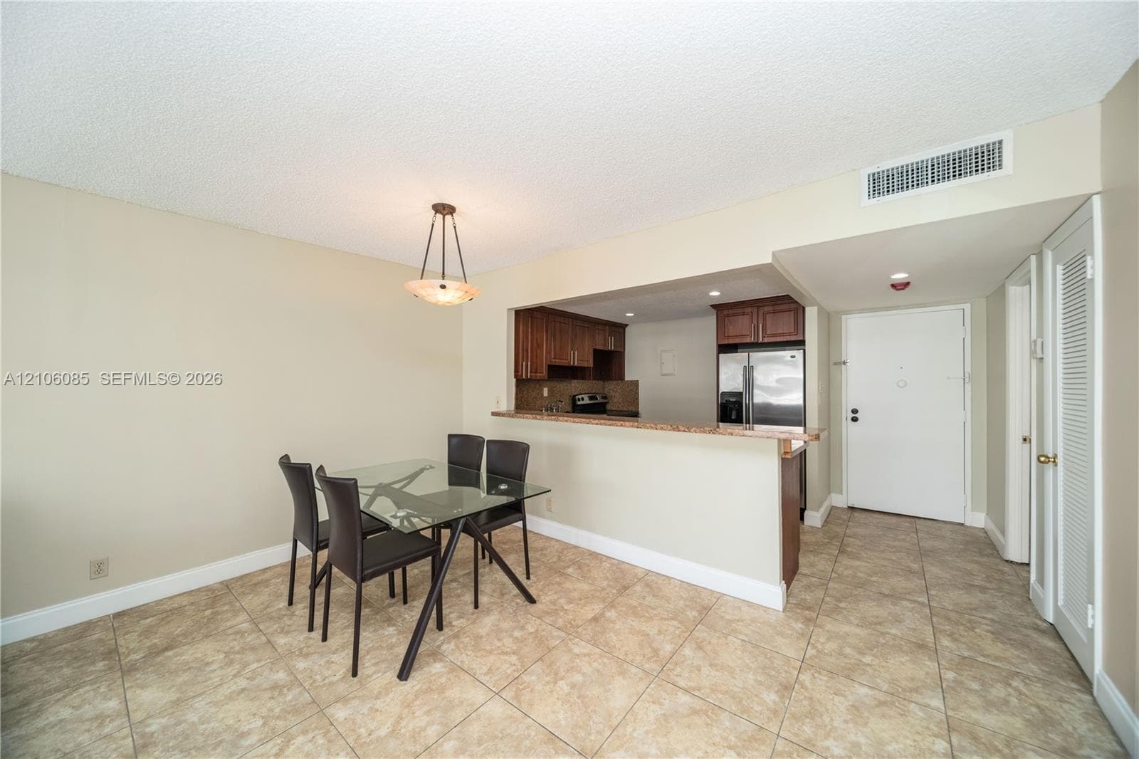Dining area featuring tile flooring, a tiered pendant light fixture, and a pass-through opening to the kitchen with wood cabinetry and countertop seating
